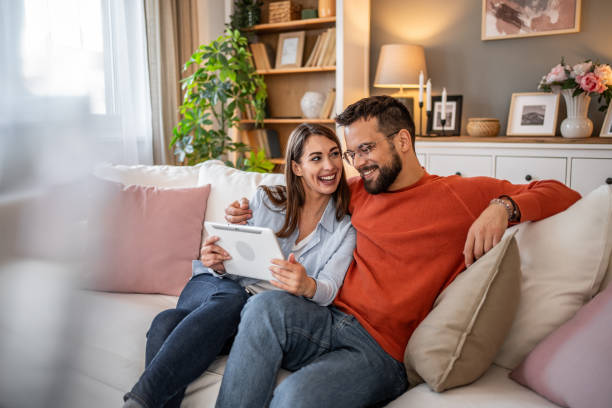 istock A couple laughs while using a digital tablet together at home. Boy and girl relaxing and using social media on digital tablet in living room at home 2166907864