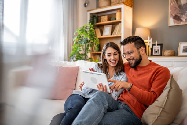 istock A couple laughs while using a digital tablet together at home. Boy and girl relaxing and using social media on digital tablet in living room at home 2166908116