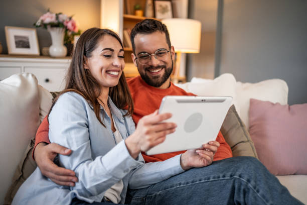 istock A couple laughs while using a digital tablet together at home. Boy and girl relaxing and using social media on digital tablet in living room at home 2166908165