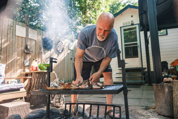 istock Mature man roasting chicken wings on outdoor fire pit BBQ 2166910452