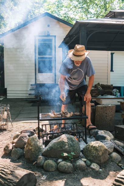 istock Mature man roasting chicken wings on outdoor fire pit BBQ 2166910534