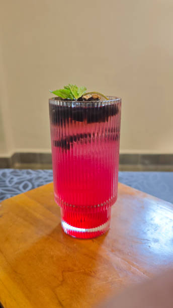 Refreshing Layered Raspberry and Coconut Water Beverage with Grass Jelly and Citrus Garnish in a Textured Clear Glass on a Wooden Table