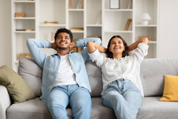 istock Content indian couple relaxing on sofa with hands behind head 2166926108