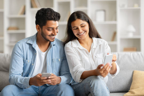 istock Happy indian couple browsing on phone, relaxed at home 2166926117