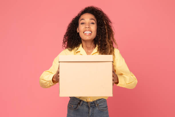 istock Young black woman smiles holding parcel on pink backdrop 2166926316
