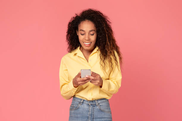 istock Happy black woman using cellphone, smiling, posing on pink background 2166926318