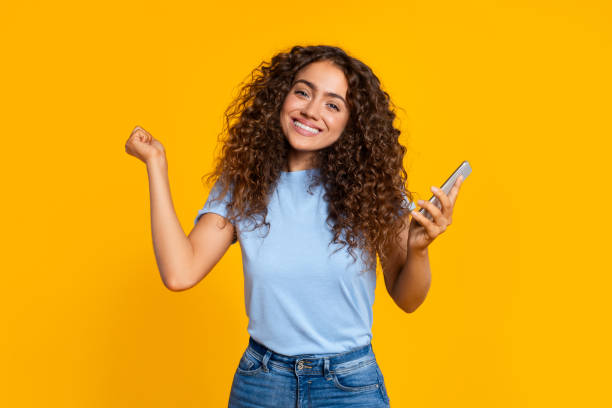 istock Happy woman with smartphone celebrating on yellow 2166926367