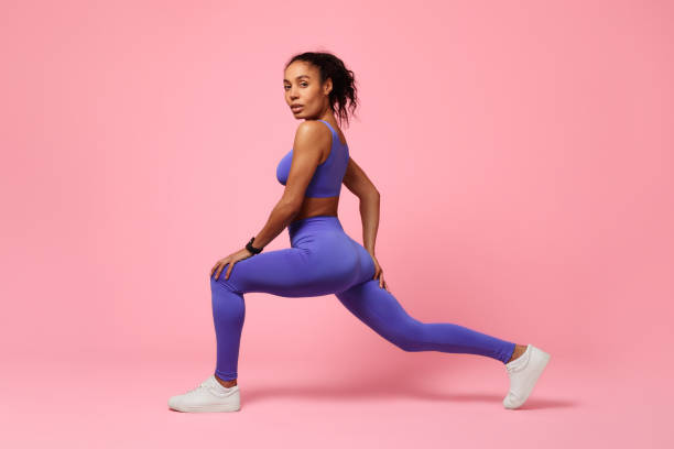 istock Sporty black woman lunging forward exercising over pink studio background 2166927539