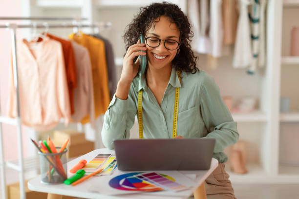 Smiling designer multitasking with phone and laptop