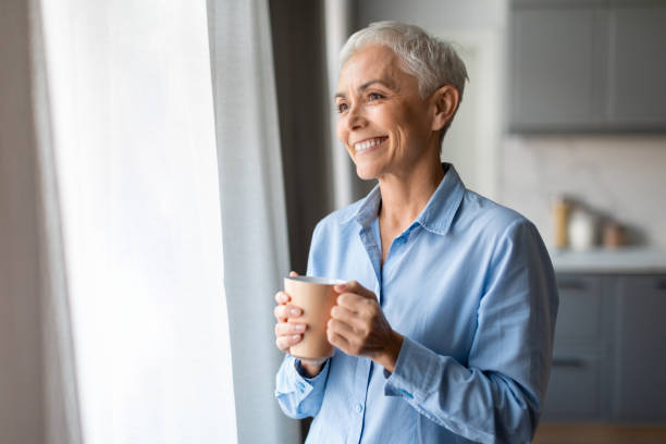 istock Senior lady holds cup with hot beverage standing indoor 2166927857