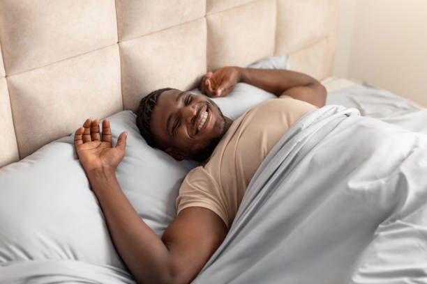 istock Well rested black man wakes up stretching arms in bed 2166928092