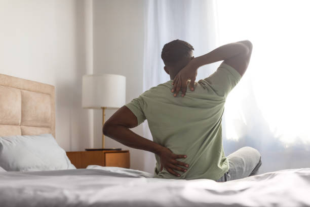 istock african man sitting on bed touching sore back and neck 2166928116