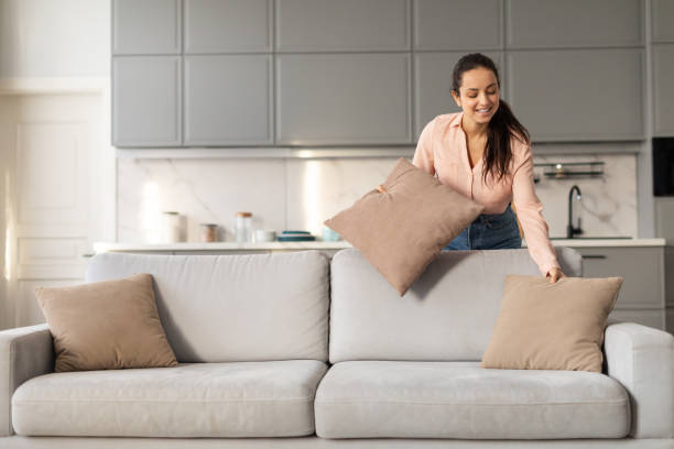 istock Happy lady arranging pillows on stylish couch at home 2166928779