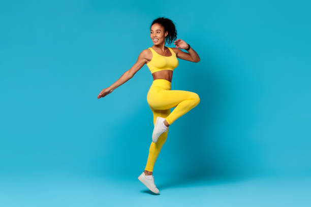 istock black woman in sportswear jumping doing exercise on blue backdrop 2166928829