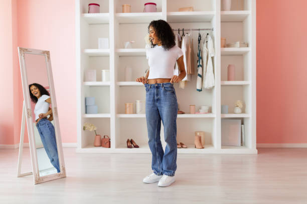 istock Happy woman trying on oversized jeans at home, mirror reflection 2166928857