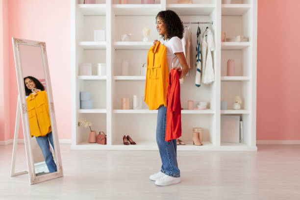 istock Woman choosing between yellow and red tops, mirror view 2166928858