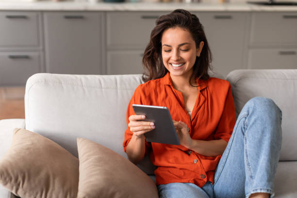 Smiling woman browsing on tablet, lounging on sofa