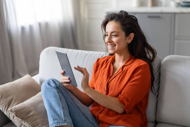 istock Smiling woman in orange shirt using tablet on comfortable sofa at home 2166929169