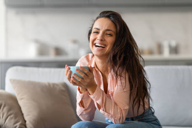 istock Joyful woman laughing while holding cup, in cozy home setting 2166929171