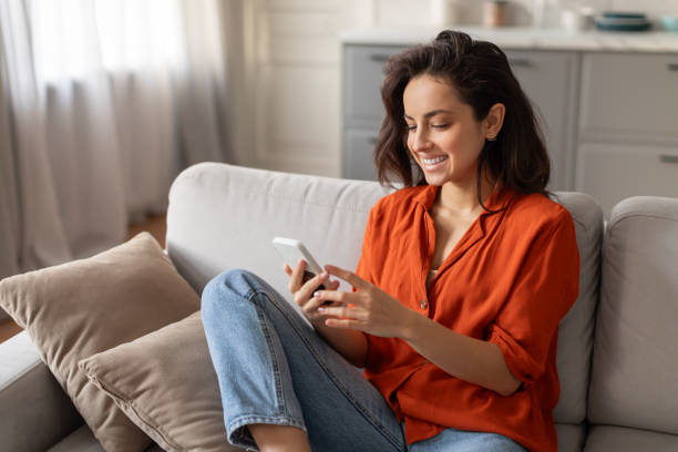 istock Smiling young woman browsing cellphone on sofa 2166929190