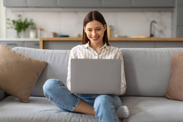 istock Happy woman using laptop on cozy sofa at home 2166929581
