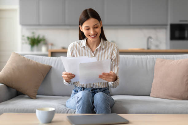 istock Happy woman reading documents on couch with laptop and tea 2166929614