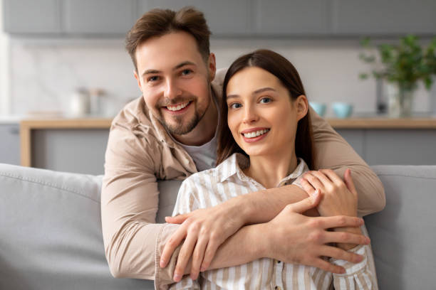 istock Happy couple embracing on the sofa and smiling at camera 2166929653