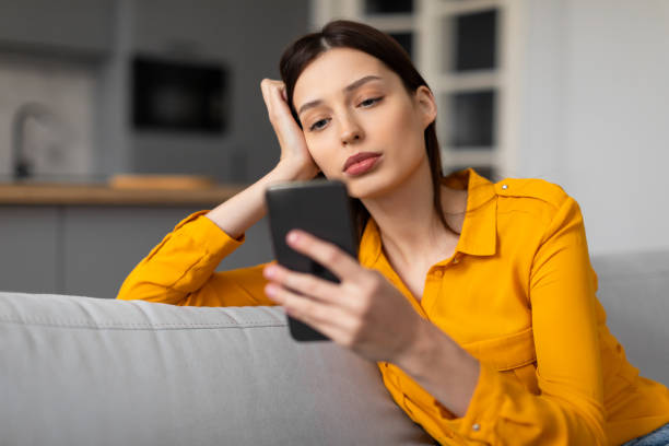istock Pensive woman with phone looking sad and thoughtful on sofa 2166929668