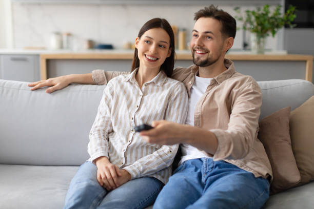 istock Smiling couple relaxing with remote on sofa, watching tv 2166929673