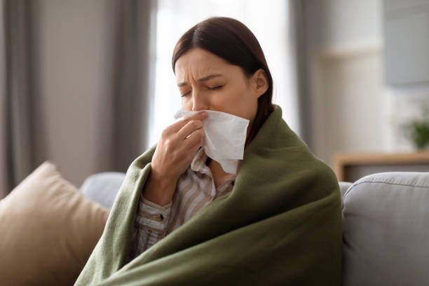 istock Sick young woman wrapped in blanket blowing her nose 2166929689
