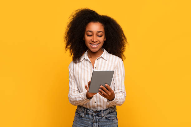 istock Smiling black woman using tablet, isolated on yellow background 2166932104