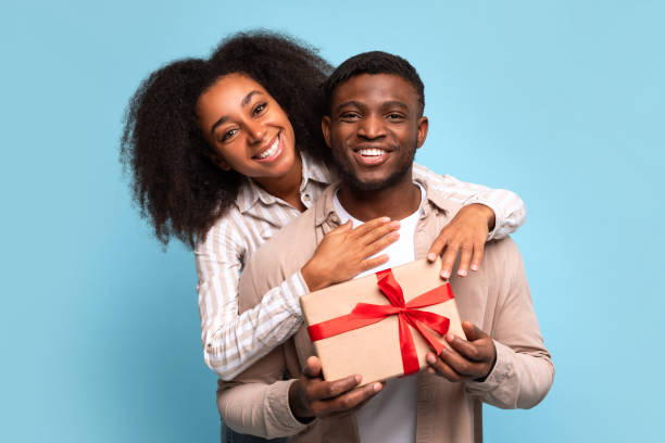 istock Joyful black couple sharing gift box with red ribbon on blue background 2166932116