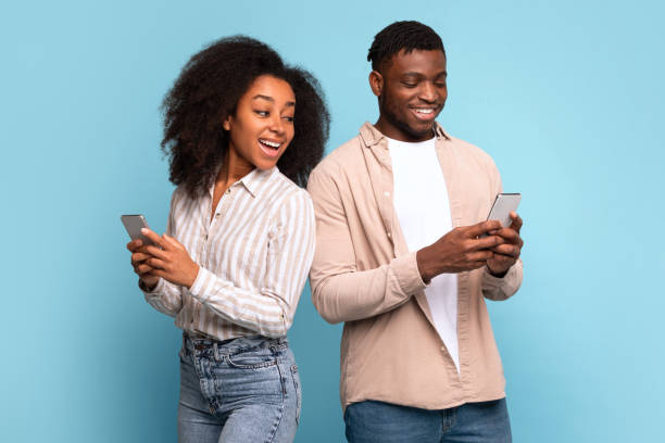 istock Happy black couple using smartphones back-to-back on light blue background 2166932118