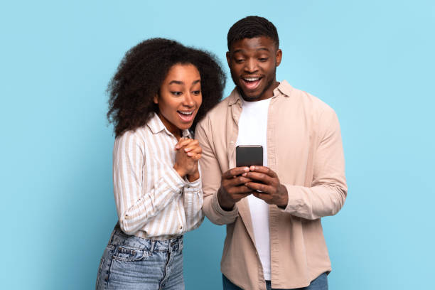 Excited black couple viewing smartphone together on blue background