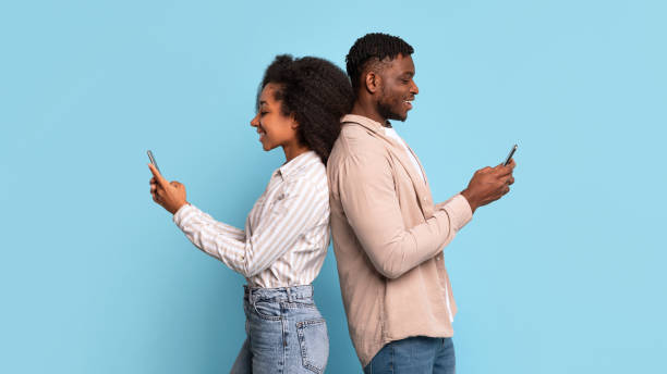 istock Black man and woman using smartphones back-to-back on blue backdrop 2166932149