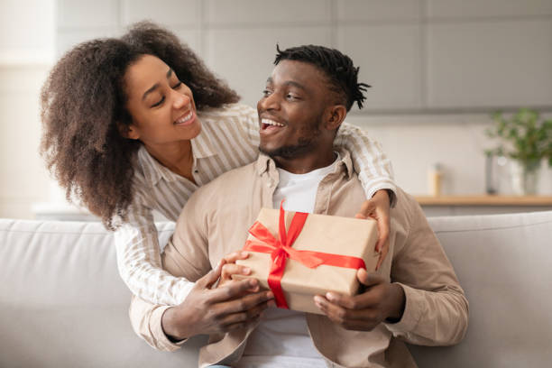 istock Cheerful black wife surprising her husband giving present box indoors 2166932442