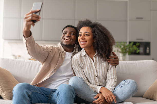 istock black couple making selfie shot sitting on sofa at home 2166932550
