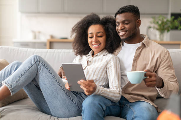 istock Smiling black couple relaxing with tablet computer on couch indoor 2166932551