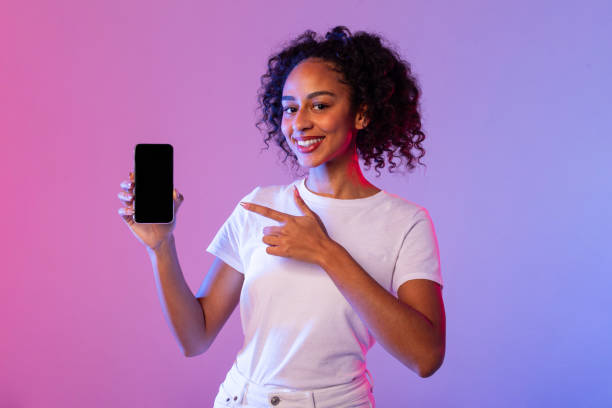 istock Happy woman pointing at smartphone with blank screen, neon backdrop 2166933420