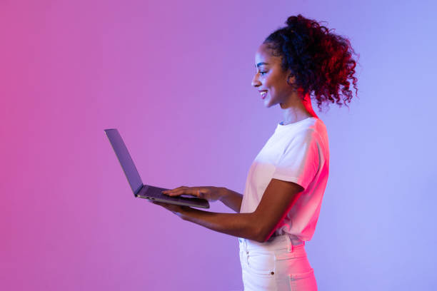 istock Smiling black woman using laptop with neon light background 2166933421