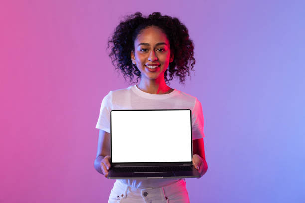 istock Cheerful black woman presenting laptop with blank screen on neon background 2166933424
