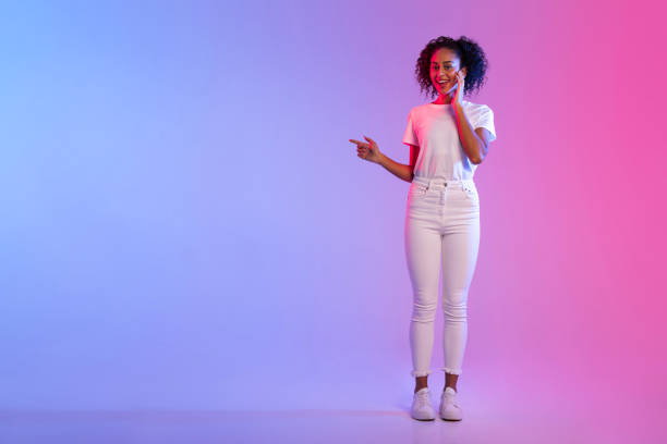 istock Smiling black lady pointing to side at free space on blue and pink gradient background 2166933448