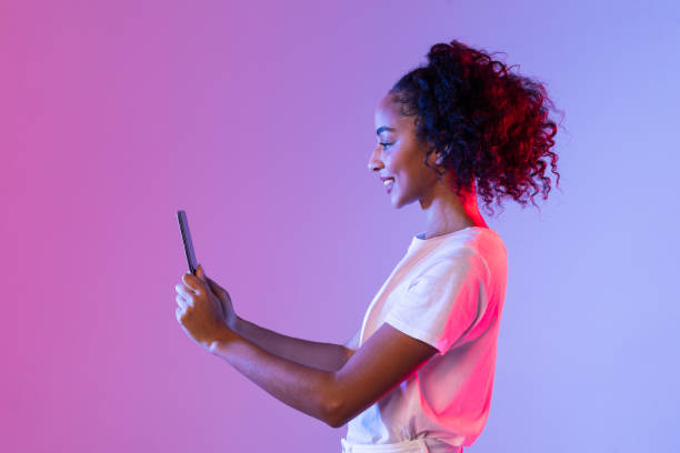 istock Smiling black woman using tablet on neon two-toned background 2166933454