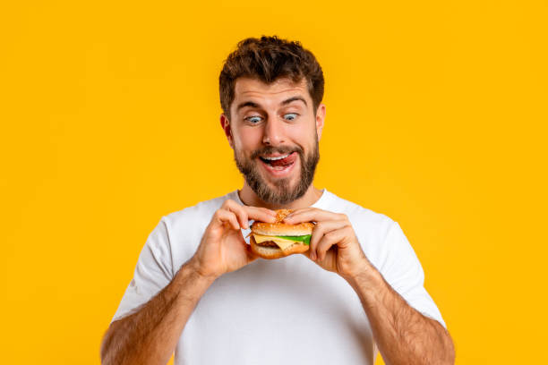 istock Joyful Hungry Young Guy Eating Burger Posing On Yellow Background 2166933796