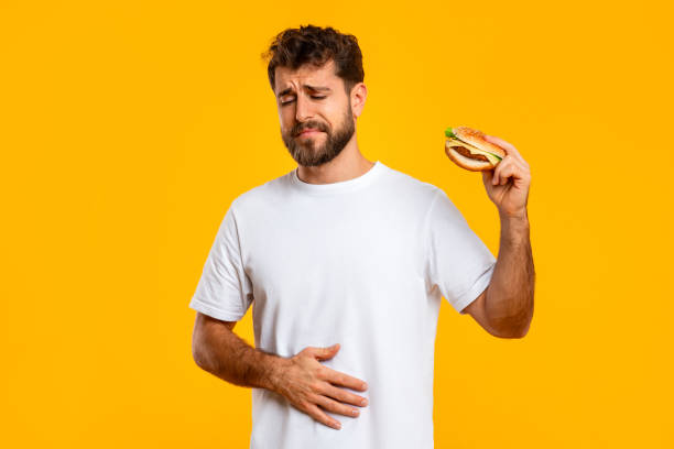 istock Upset Man Touching Aching Stomach Holding Burger Over Yellow Background 2166933801