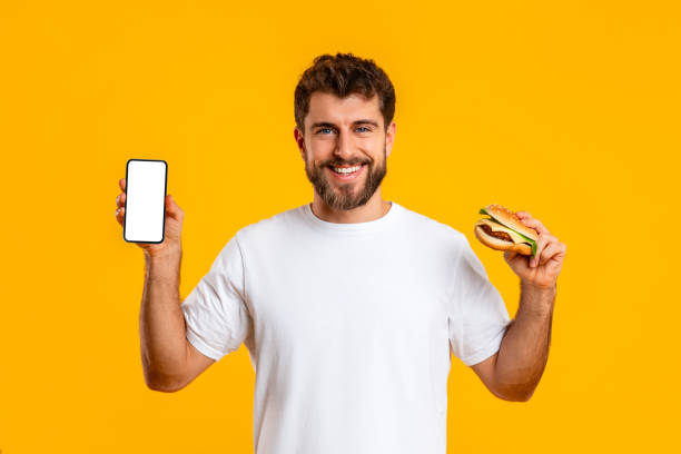 istock Happy guy holds burger and shows phone empty screen, studio 2166933803