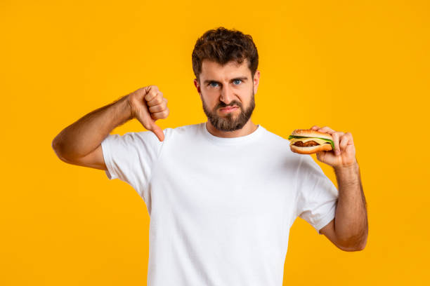 istock Man Holding Burger Gesturing Thumb Down Disapproving Unhealthy Nutrition, Studio 2166933809