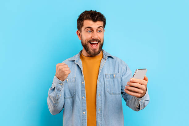 istock Joyful caucasian guy holding smartphone and gesturing yes, blue background 2166933833