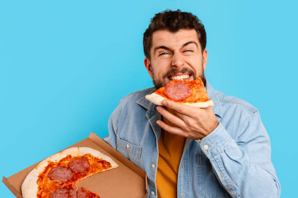 istock Funny Man Eating Pizza Standing Holding Box Over Blue Background 2166933836