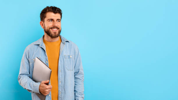istock Happy young man holding his laptop computer on blue background 2166933838